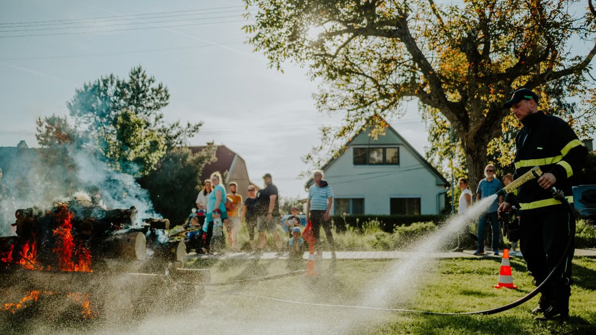 A firefighter extinguishes a controlled fire as a crowd watches during a demonstration on a sunny day.